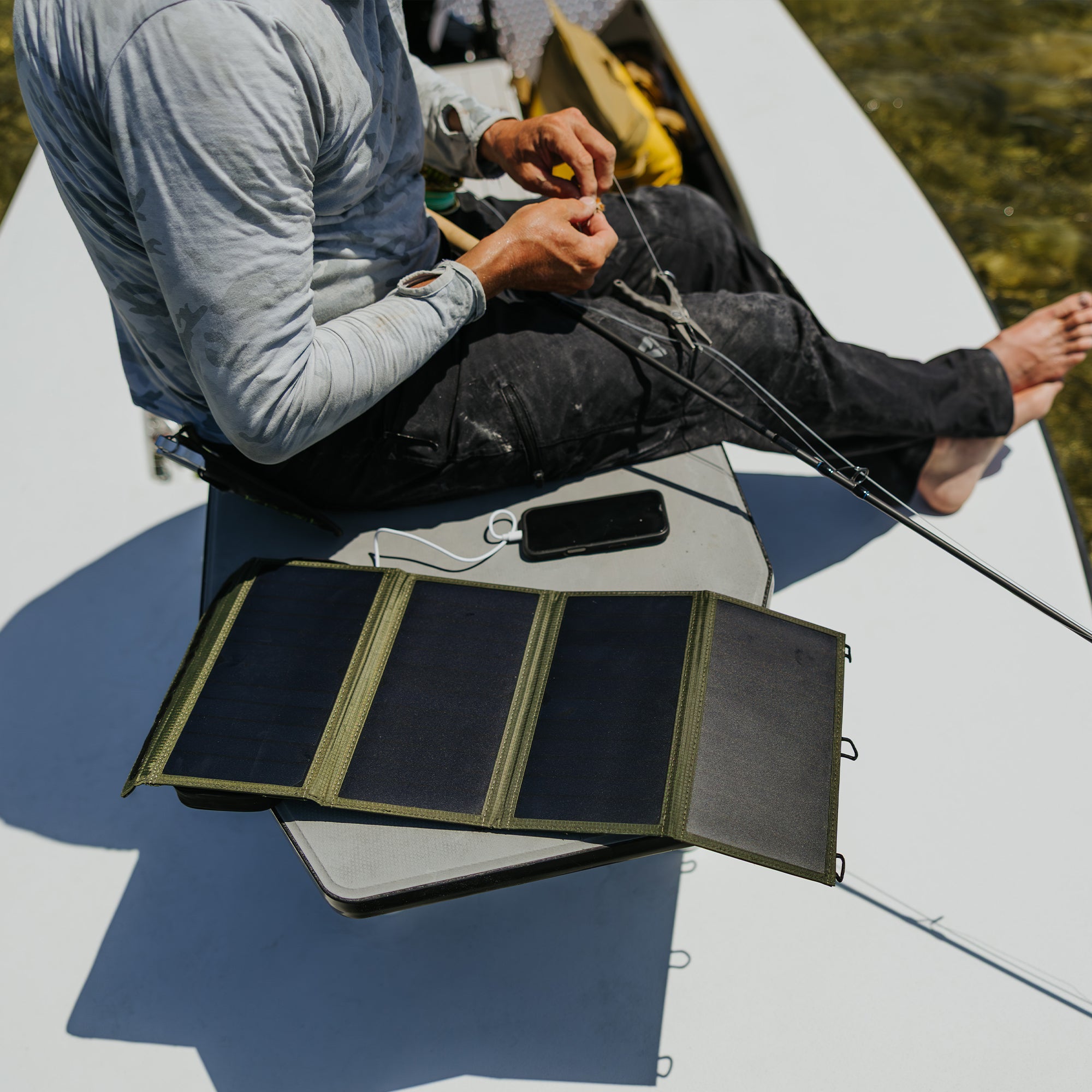 a wet nestout olive green 4 solar panel unfolded and charging a smartphone with fisherman sitting next to it on small boat