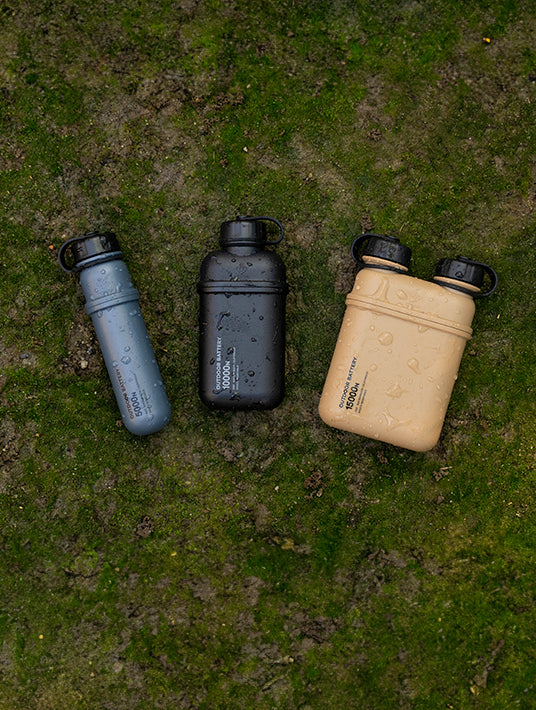 Three outdoor batteries in gray, black, and beige on a green mossy surface