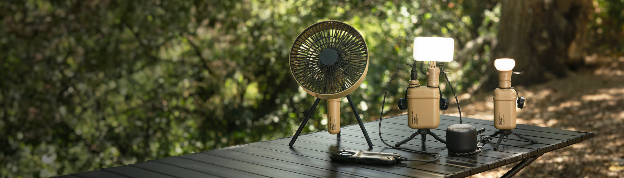 three outdoor batteries with lights and fan attachments sit on camping table outside