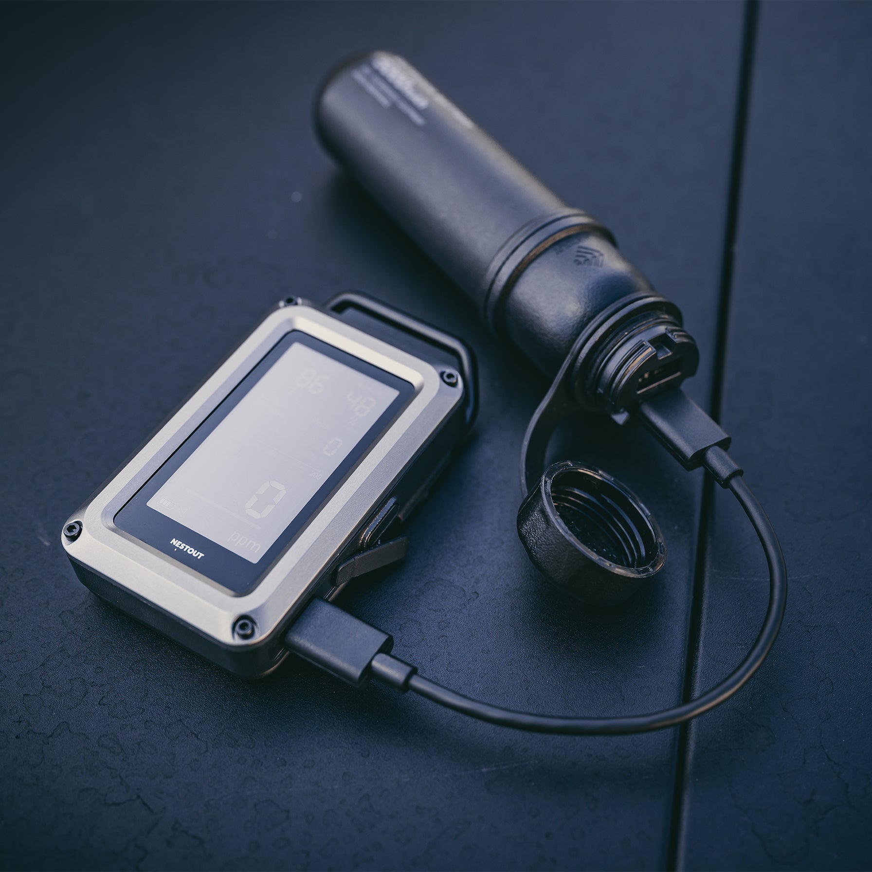 CO monitor being charged by a 5000mAH NESTOUT power bank on a dark surface