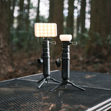 image of the nestout black flash attached to the black 5k nestout battery standing on tripod next to the nestout black lamp connected to black 5k battery standing on tripod on a table in the woods