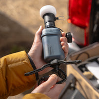 Image of hand holding nestout black lamp with spacer attached 10k grey battery with opened tripod attached