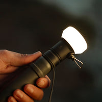 Image of hand holding a turned on nestout black lamp attached to 5k battery