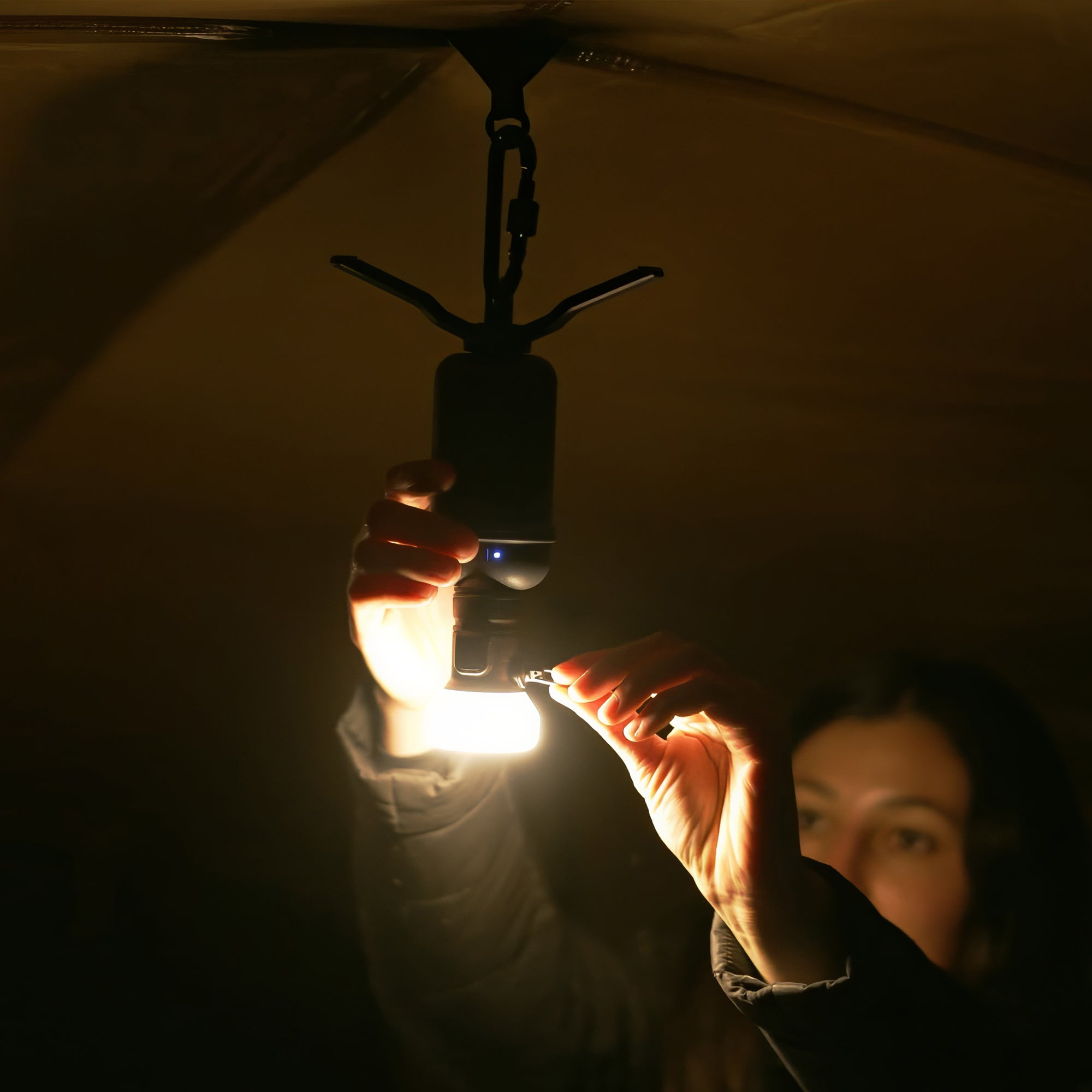 Image of woman hiker turning on nestout lamp attached to 10k battery hanging upside down inside a tent