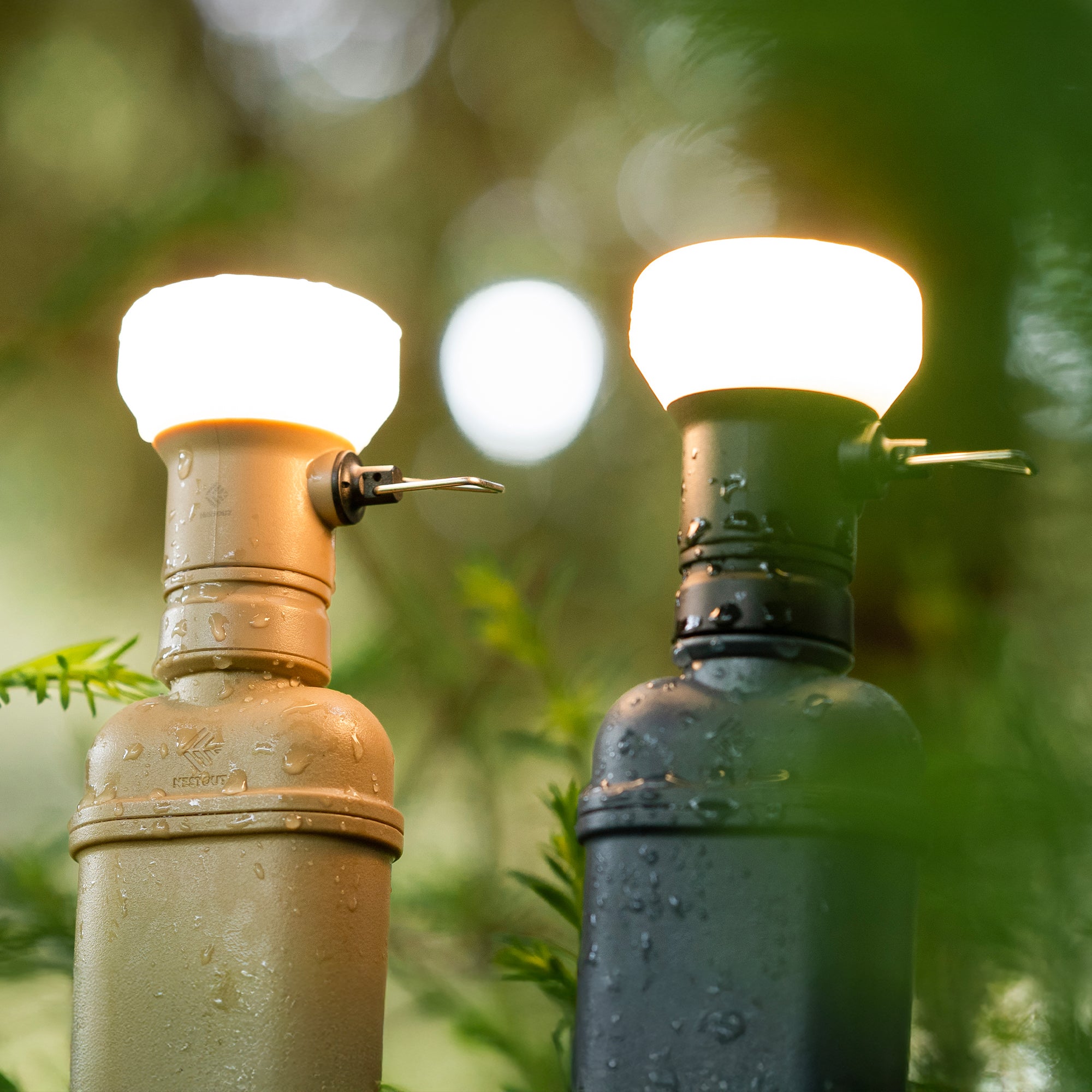 Image of wet turned on nestout beige lamp and black lamp with spacer attached to 10k batteries in the woods