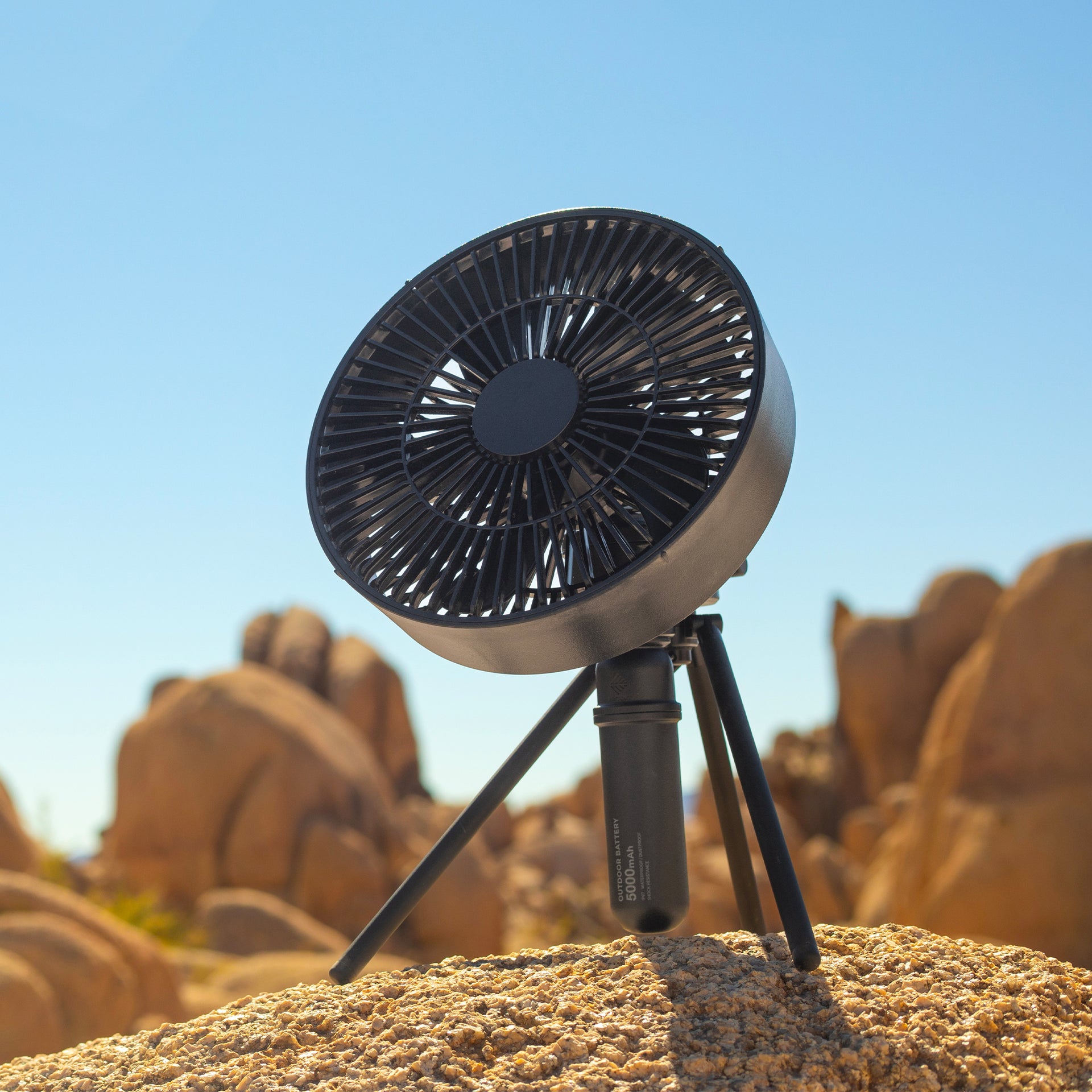 Image of female hiker sitting on rocks in joshua tree with black fan with black tripod attached and 5k battery attached