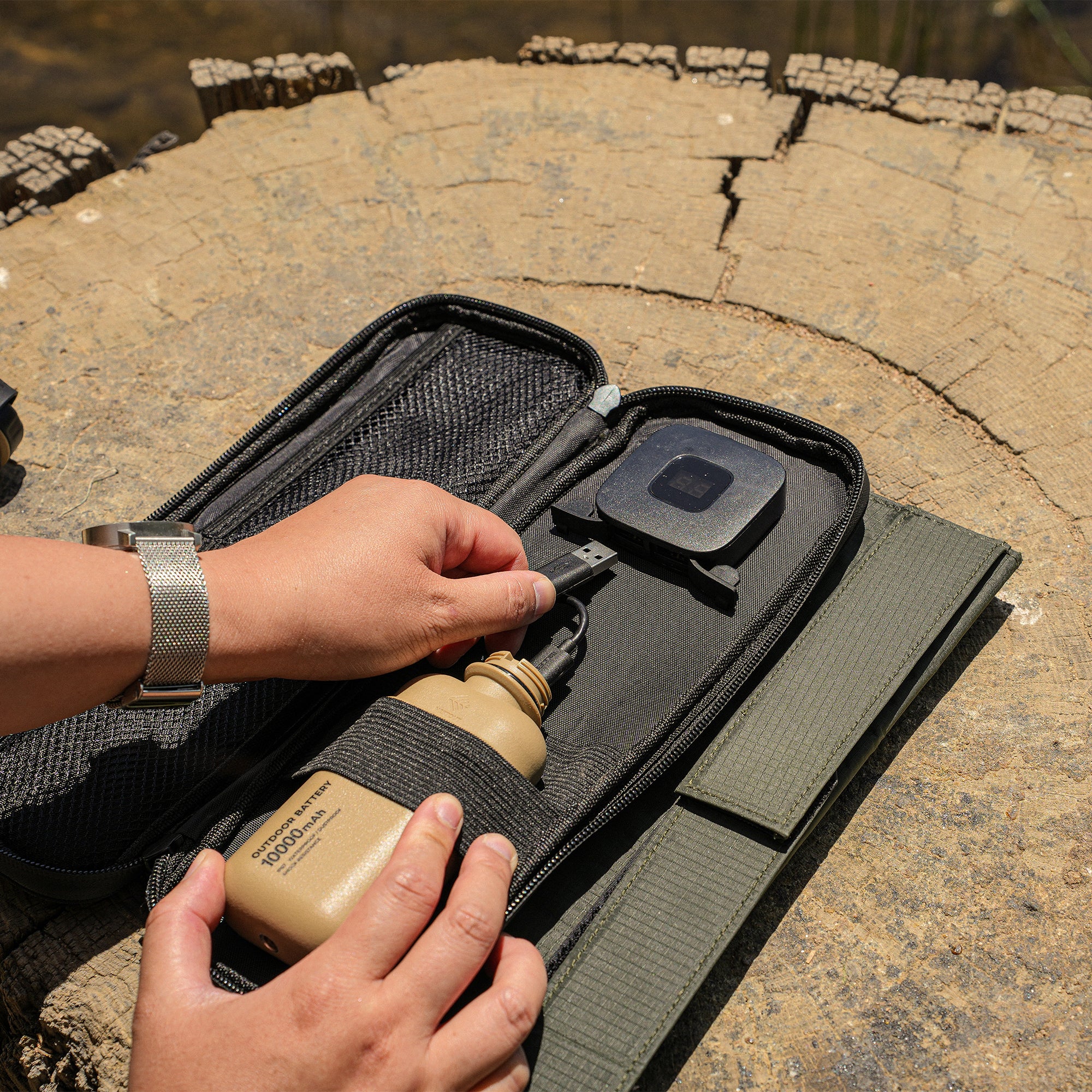 image of  hands connecting the nestout beige 10k battery into the nestout olive green 2 solar panel USB connector resting on a tree stump in Jens Lake
