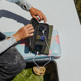 image of hands holding open the nestout olive green 4 solar panel with the USB connector connected to a smartphone out fishing