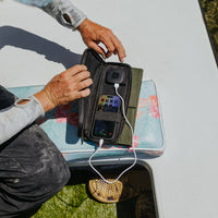 image of hands holding open the nestout olive green 4 solar panel with the USB connector connected to a smartphone out fishing