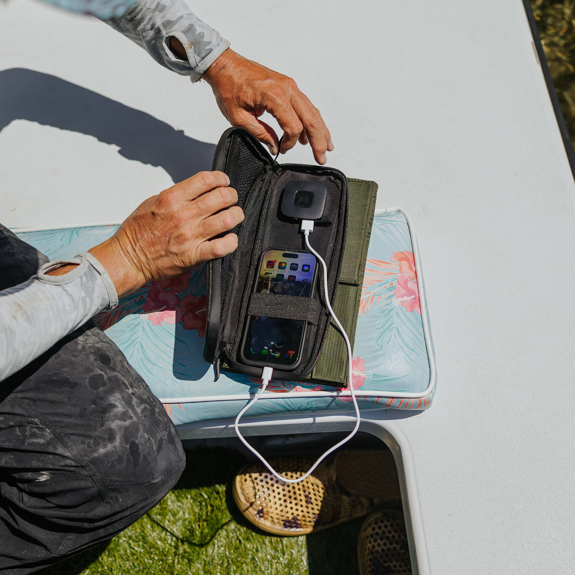 image of hands holding open the nestout olive green 4 solar panel with the USB connector connected to a smartphone out fishing