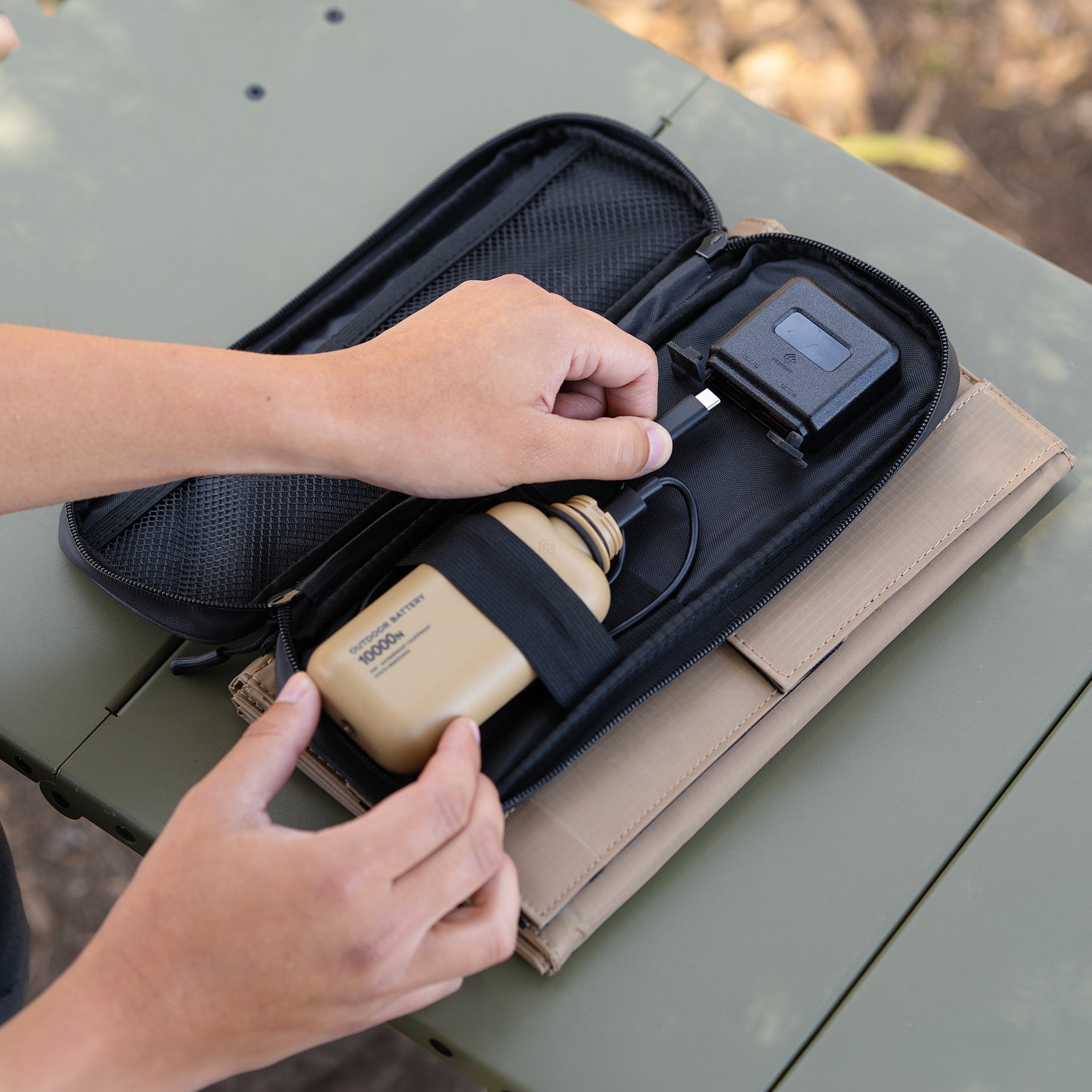 Person plugging power bank into solar panel usb-c port on a table in the outdoors