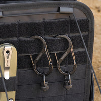 Close-up of two black metal carabiners with quick-release buckles hanging from a black tactical gear case
