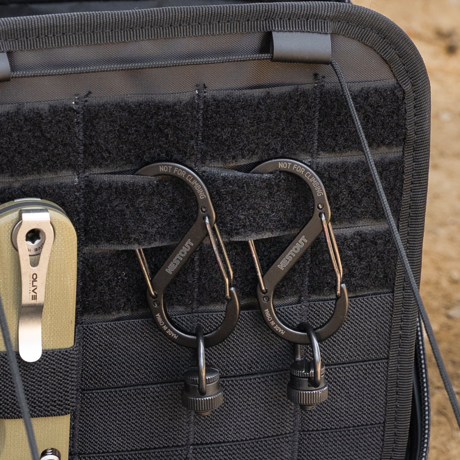 Close-up of two black metal carabiners with quick-release buckles hanging from a black tactical gear case