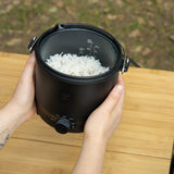 black outdoor cooker with freshly cooked steam rice inside of it.