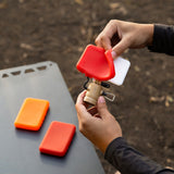 person holding a flash-1 light attachment and attaching a red light filter and two other filters on a table