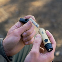 image of hiker hands placing the AAA battery into the nestout beige whistle light
