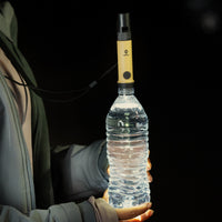 image of hiker in the dark holding a water bottle with the nestout beige light turned on and placed into the opening of the bottle in order to expand light