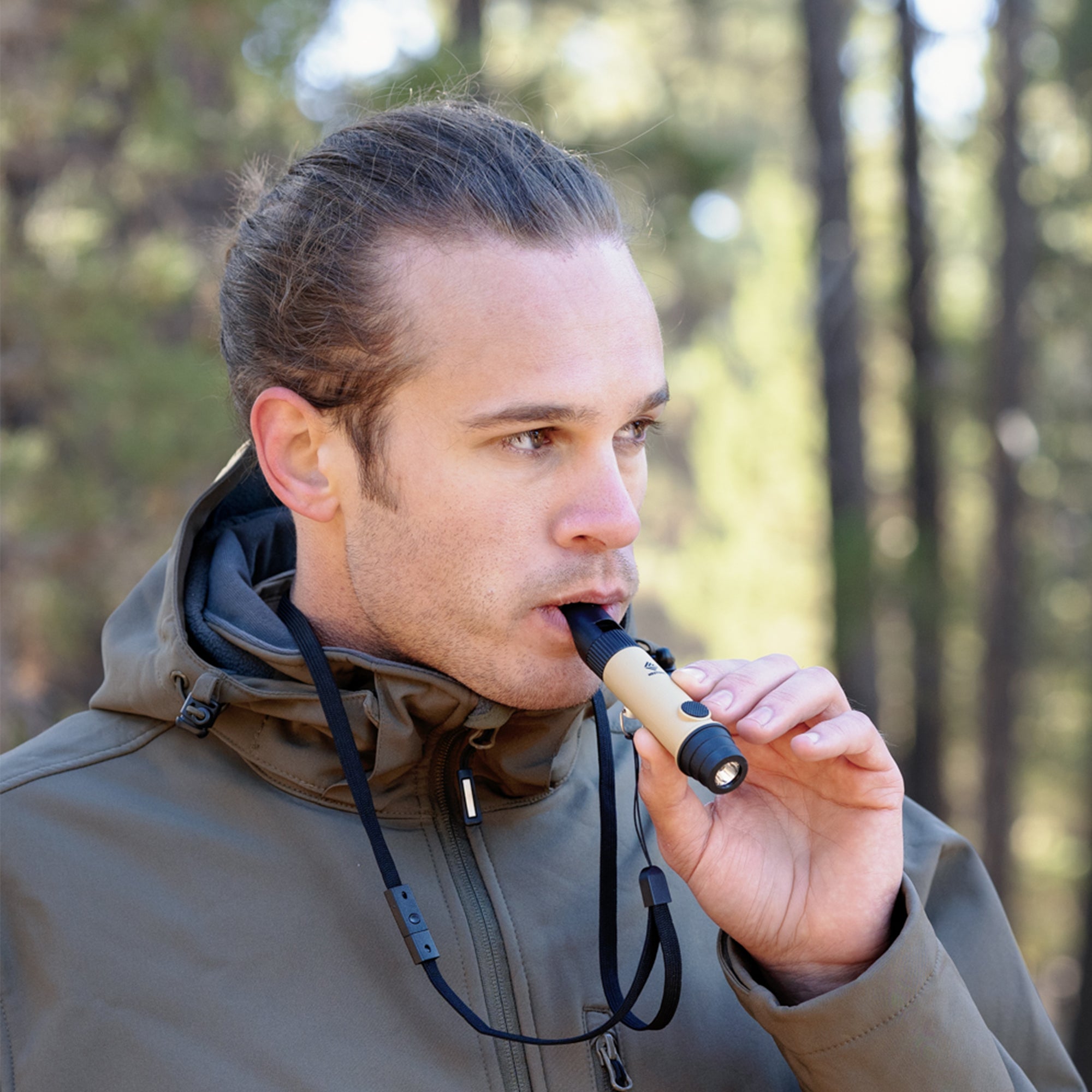 image of male hiker blowing on the nestout beige whistle which is hanging from his neck from the lanyard