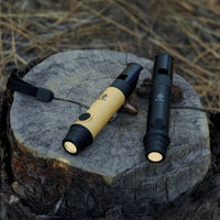 image of the nestout black and beige whistle lights turned on and resting on a tree stump with hay on the ground