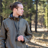 image of hiker in the woods looking to the side holding the nestout black whistle light which is hanging from his neck from the lanyard 