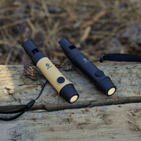 image of the nestout black and beige whistle lights turned on and resting on wood with hay on the ground