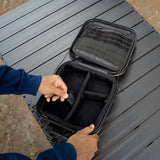 Person opening a black travel case on a gray surface