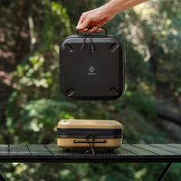 Person holding a gear case on a wooden table with greenery in the background