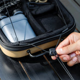 Person securing a black strap on a black and beige case with camping gear inside.