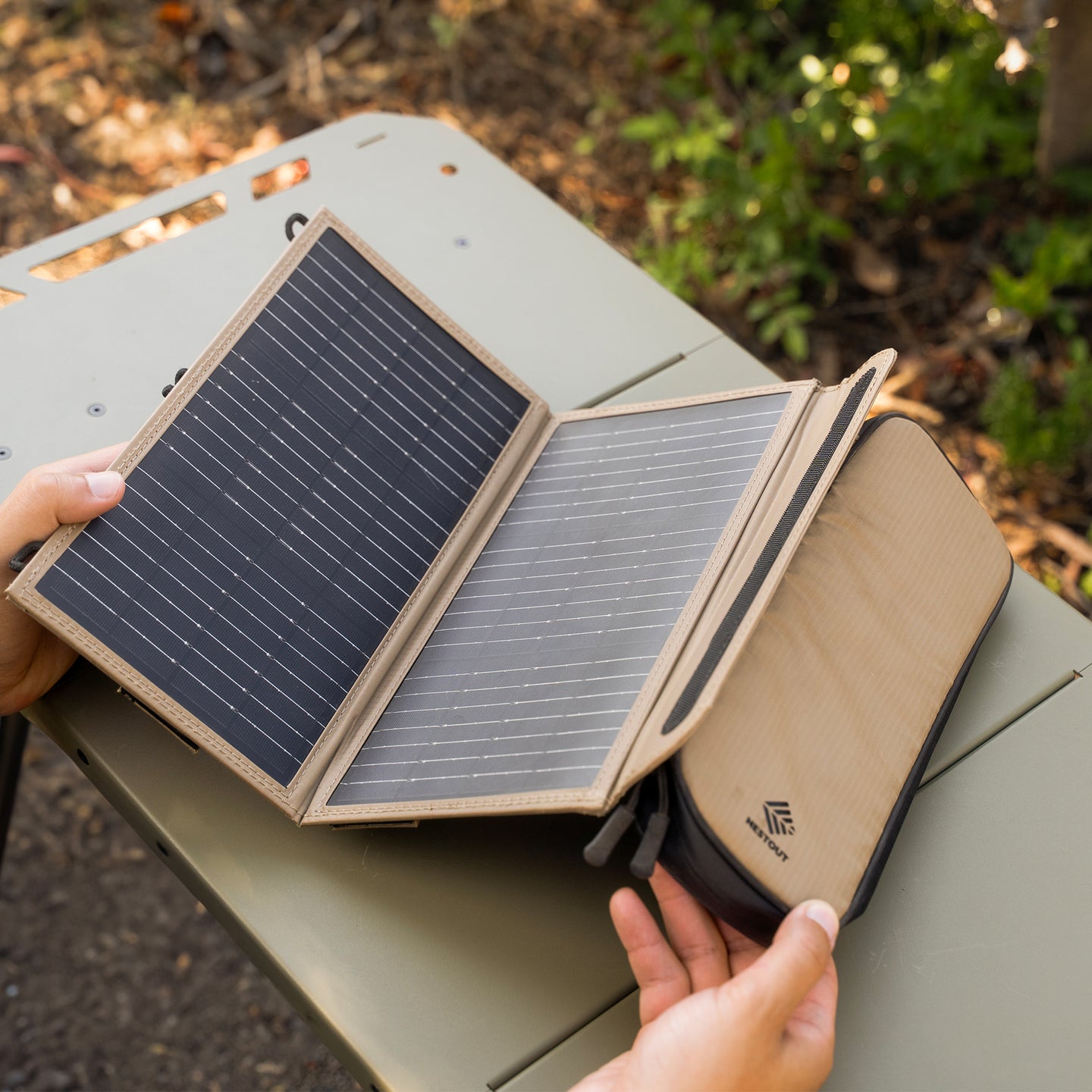 Foldable solar panel being held over a green surface with a blurred natural background