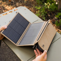 Foldable solar panel being held over a green surface with a blurred natural background