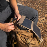 Person attaching a solar panel to backpack outdoors