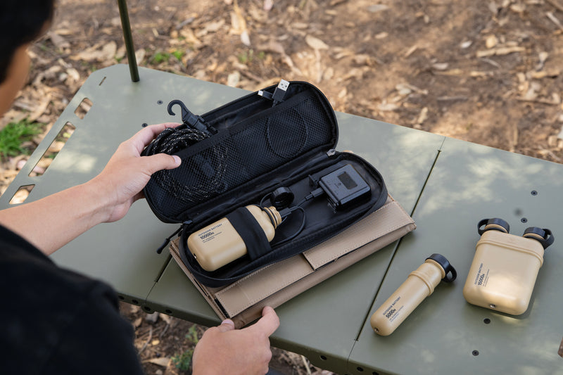 person opening the solar panel which shows a power bank being charged along with two other power banks on the side on a table outside