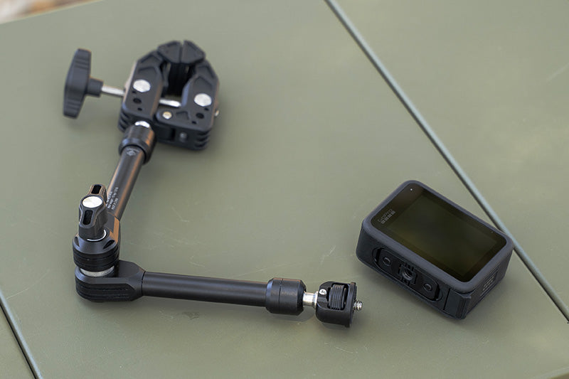 adjustable black arm clamp on a green table next to a action camera