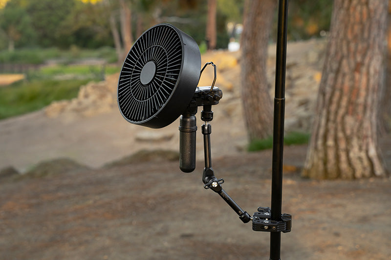 black arm clamp attached to a black pole and the clamp has a 5k power bank and fan attached outdoors
