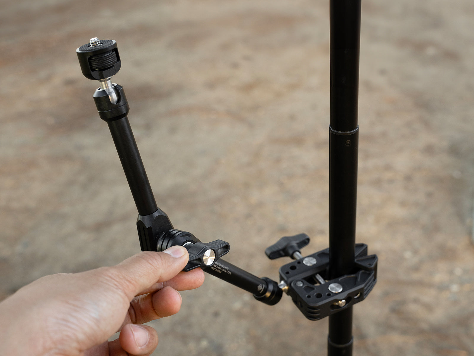 hand adjusting the black arm of a clamp that is attached to a pole outdoors