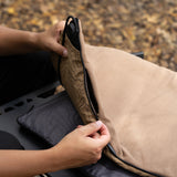 A close-up of a person's hands unzipping a beige heating pad's removable cover to show the black heating unit inside, outside on a fall day.