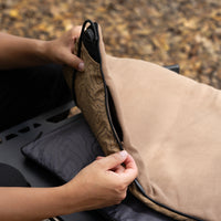A close-up of a person's hands unzipping a beige heating pad's removable cover to show the black heating unit inside, outside on a fall day.