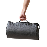 A hand carries a rolled-up gray heating pad with a topographic contour pattern by its handle, shown on a white background.