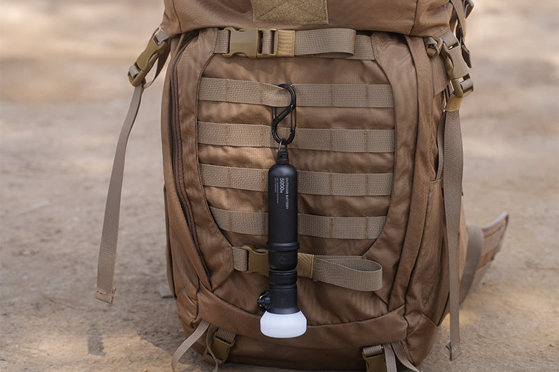 Carabiner with a 5k power bank and lamp attached, hooked onto a backpack outdoors