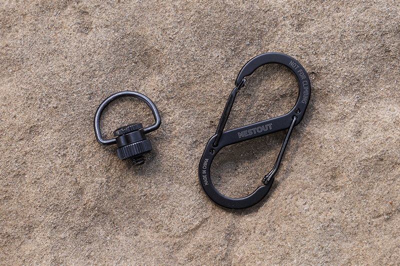 Black d-ring and carabiner clip laying on some sand outdoors