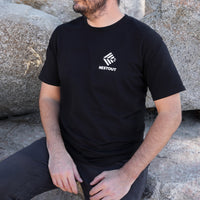 Person wearing a black t-shirt with 'NESTOUT' logo sitting against rocks.