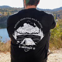 Person wearing a black t-shirt with outdoor design and Nestout logo, standing in a scenic location.