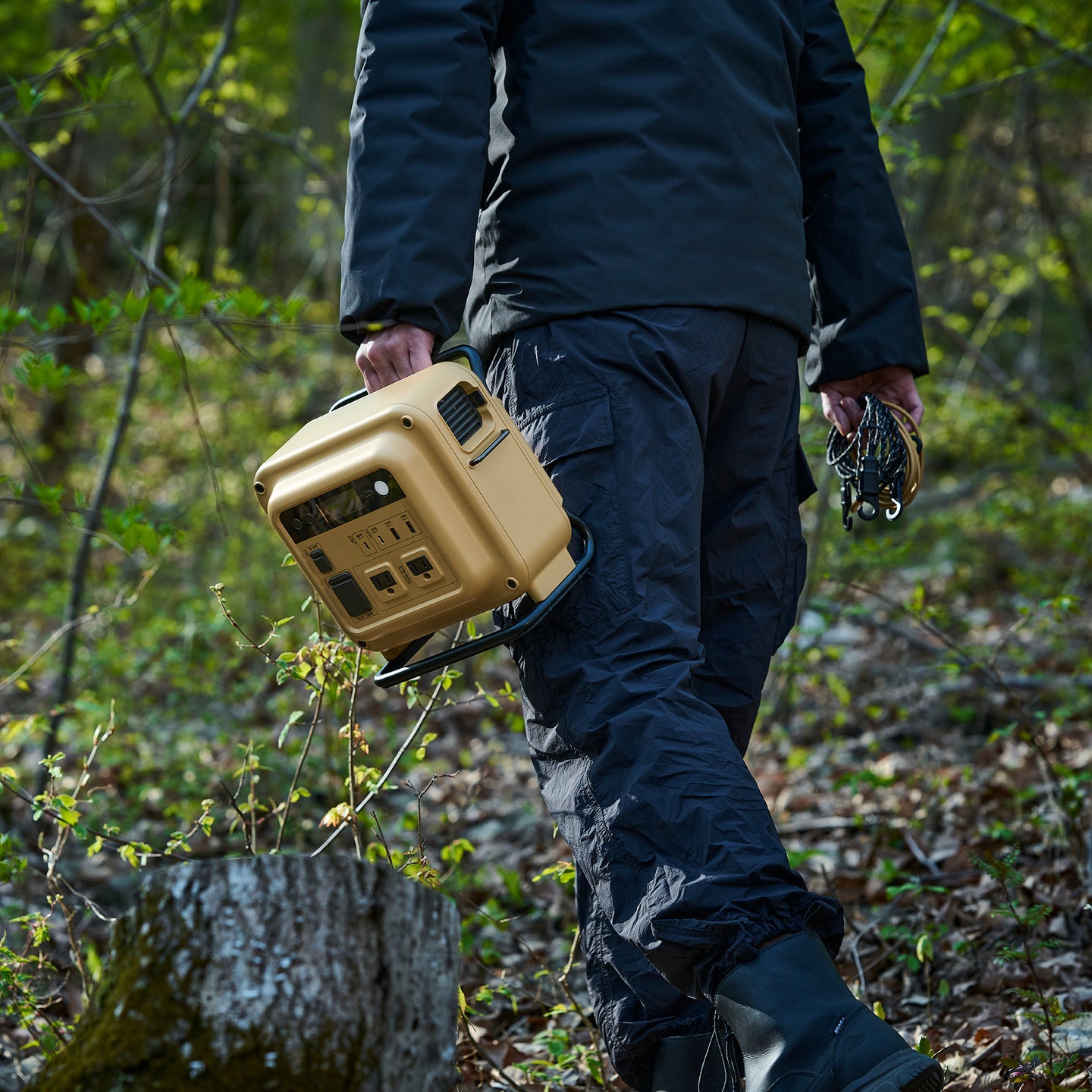 person in a park in blue camping suit carrying the nestout beige 700N power station | ultra lightweight and compact | cooling system with thermistor and washable air filter | 700W output 1300W surge | versatile 7-device charging