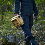 person in a park in blue camping suit carrying the nestout beige 700N power station | ultra lightweight and compact | cooling system with thermistor and washable air filter | 700W output 1300W surge | versatile 7-device charging