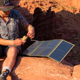 Man connecting the NESTOUT beige 10000mAh battery pack to the NESTOUT 4 panel solar charger in the Arizona cliffs