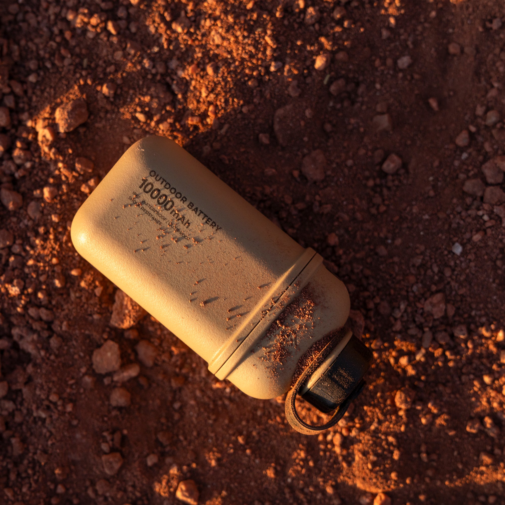 Beige colored 10000N battery pack laying in dirt 