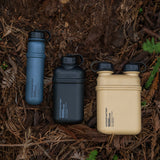 Image of nestout 10k black 5k grey 15k beige colored cylinder battery packs resting on ground in the woods | features military IP67 rating | stores up to 10000N of power | rugged waterproof design | compact size | versatile charging | to be used with NESTOUT solar panels, fans, lamps, and flashes
