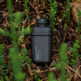 Image of nestout 10k black colored cylinder battery pack resting on shrubs | features military IP67 rating | stores up to 10000N of power | rugged waterproof design | compact size | versatile charging | to be used with NESTOUT solar panels, fans, lamps, and flashes