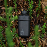 Image of nestout 10k black colored cylinder battery pack resting on shrubs | features military IP67 rating | stores up to 10000N of power | rugged waterproof design | compact size | versatile charging | to be used with NESTOUT solar panels, fans, lamps, and flashes