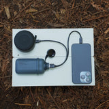 NESTOUT grey 10000mAh battery pack connected to smartphone and speaker laying on a small table in mulch